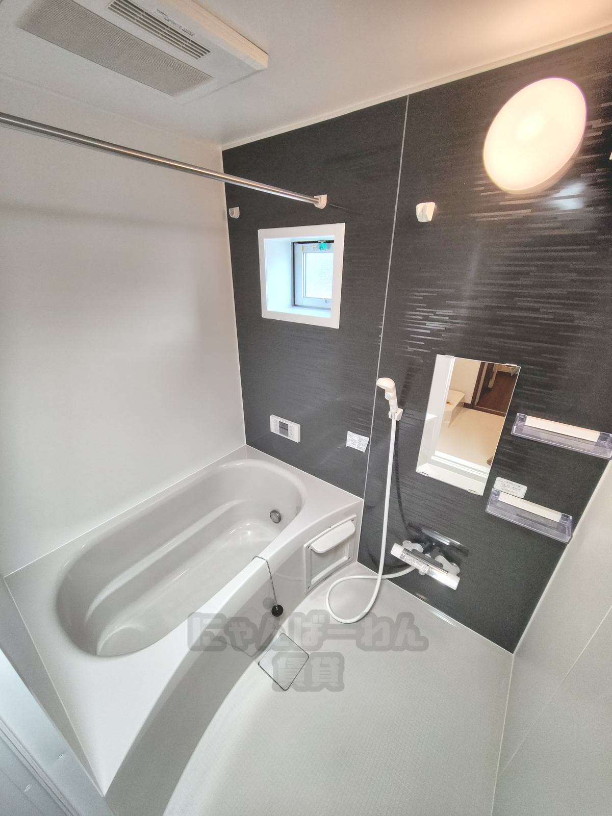 黒のアクセントパネルが特徴的なシステムバス。鏡、収納棚、追い焚き機能等が備わった浴室