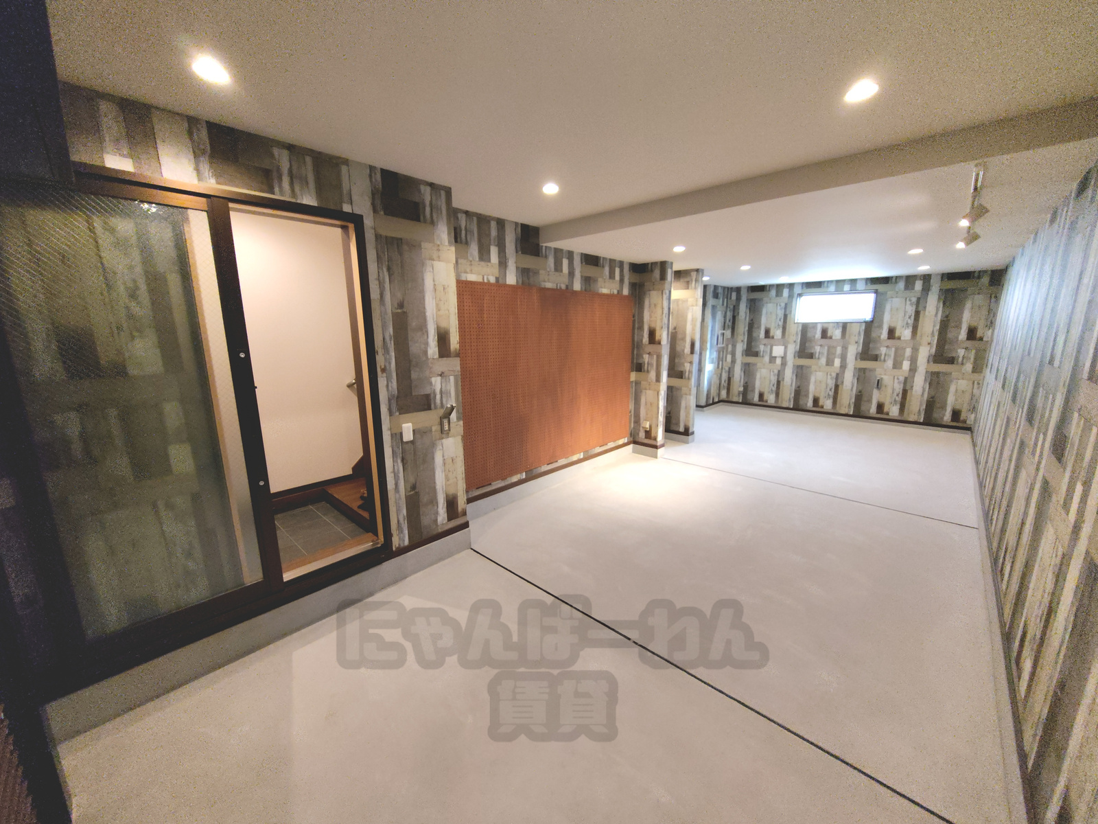 ヴィンテージ風の木目調クロスと有孔ボードが施工された、趣味や収納に便利な広い土間ガレージスペース