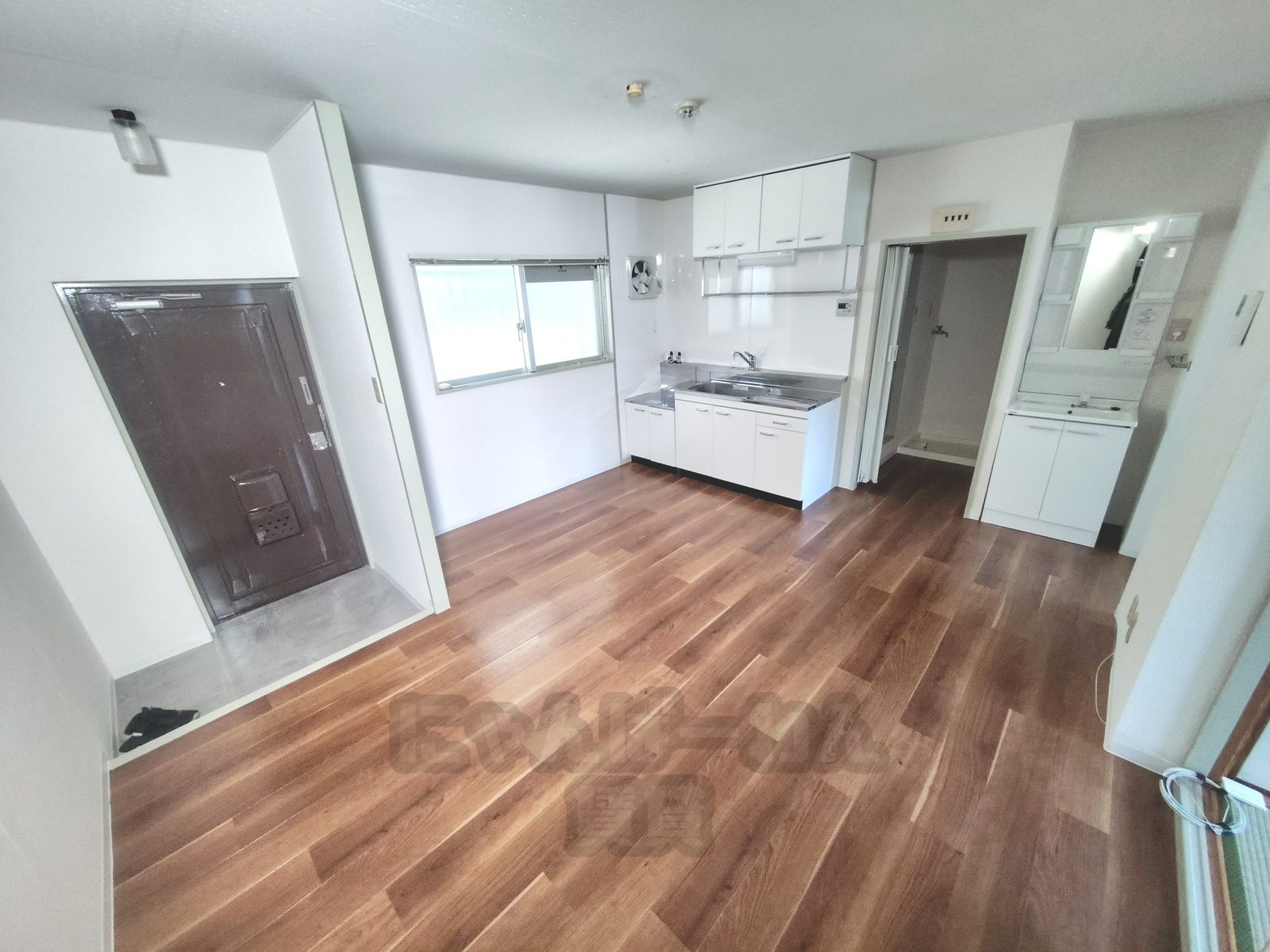 エバー・グリーン宇治弐番館105号室の木目調フローリングの居室とキッチンスペース