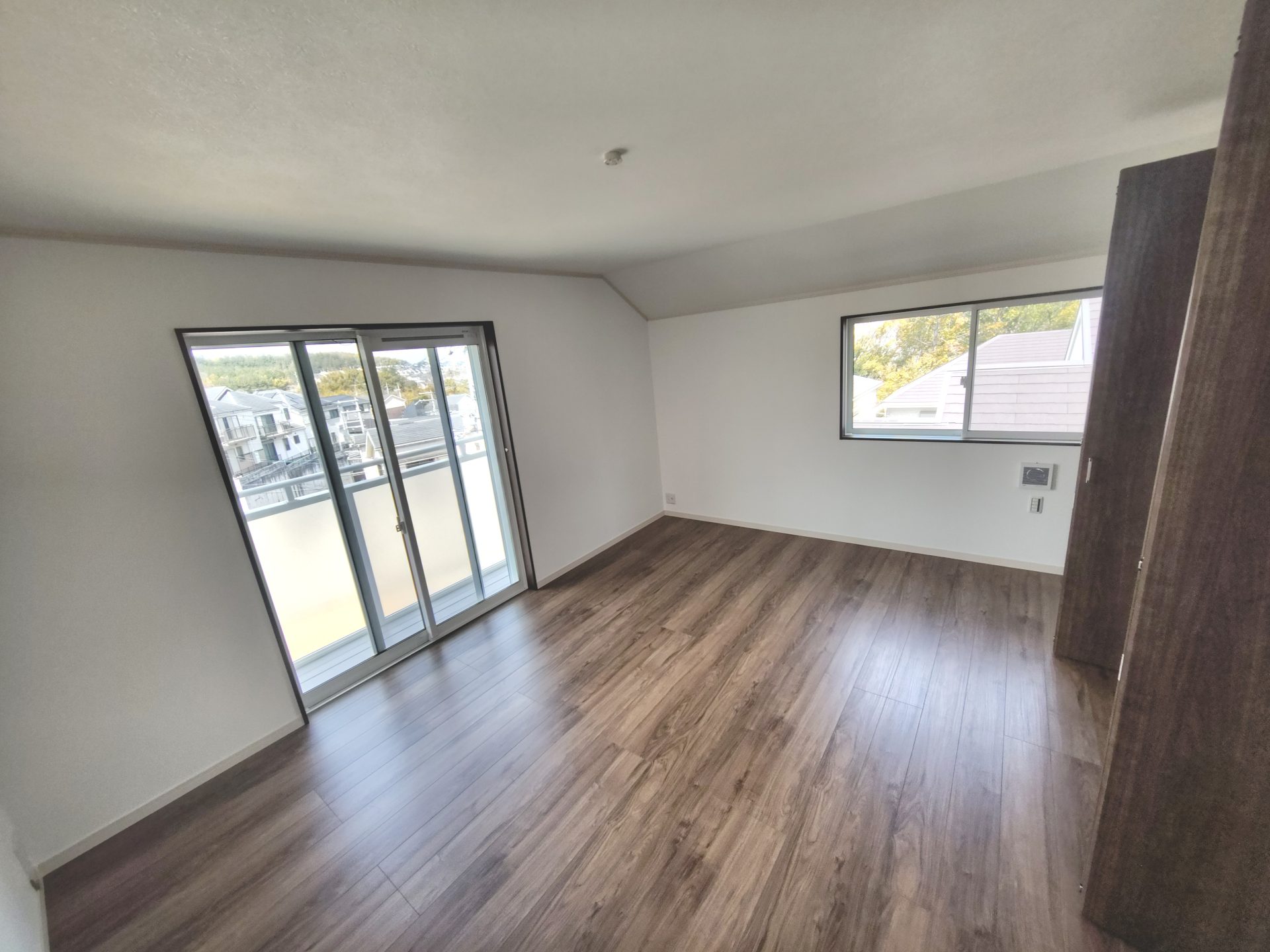 京都府京田辺市薪里ノ内のペット可賃貸物件の洋室。木目調の床と、バルコニーから住宅街が見える部屋。