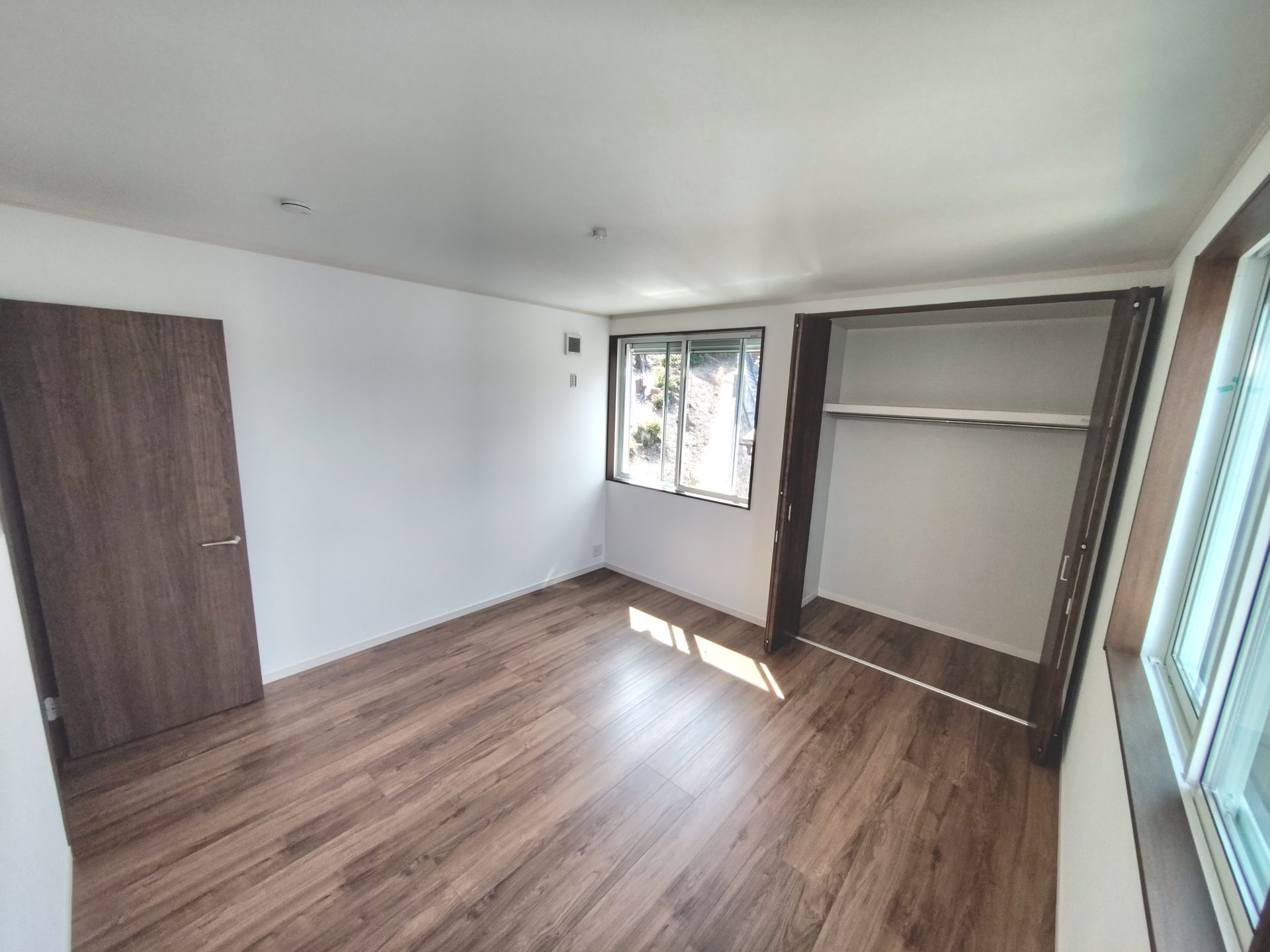 京都府京田辺市薪里ノ内のペット可賃貸物件の洋室。木目調の床とオープン状態のクローゼット、窓がある室内。