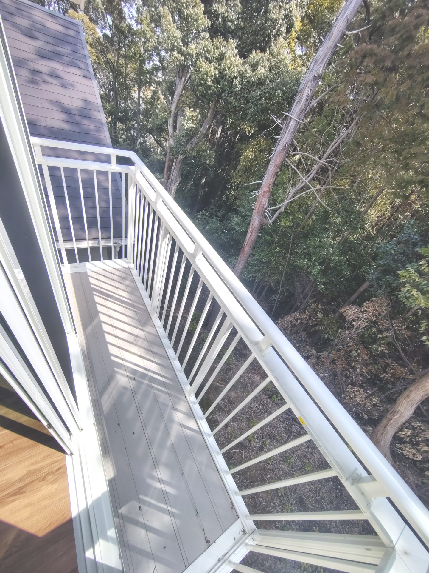 京都府京田辺市薪里ノ内の犬・猫と暮らせるペット可賃貸物件のバルコニー。白い縦格子手すりの外には木々が広がっています。