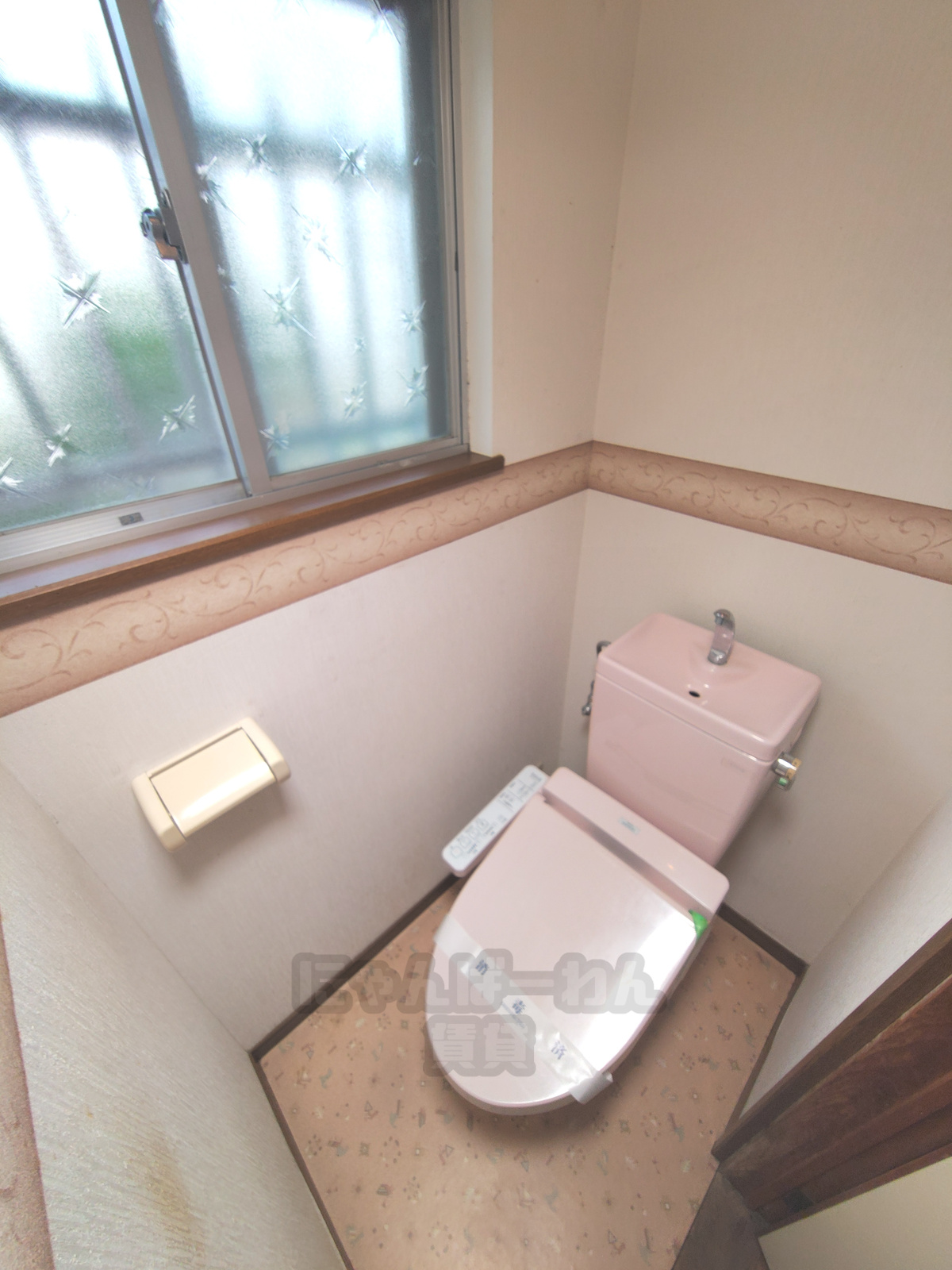 京都府宇治市木幡東中のペット可賃貸物件、ピンク色の温水洗浄便座付きトイレ。壁紙の模様、クッションフロア、窓、ペーパーホルダーが見える。