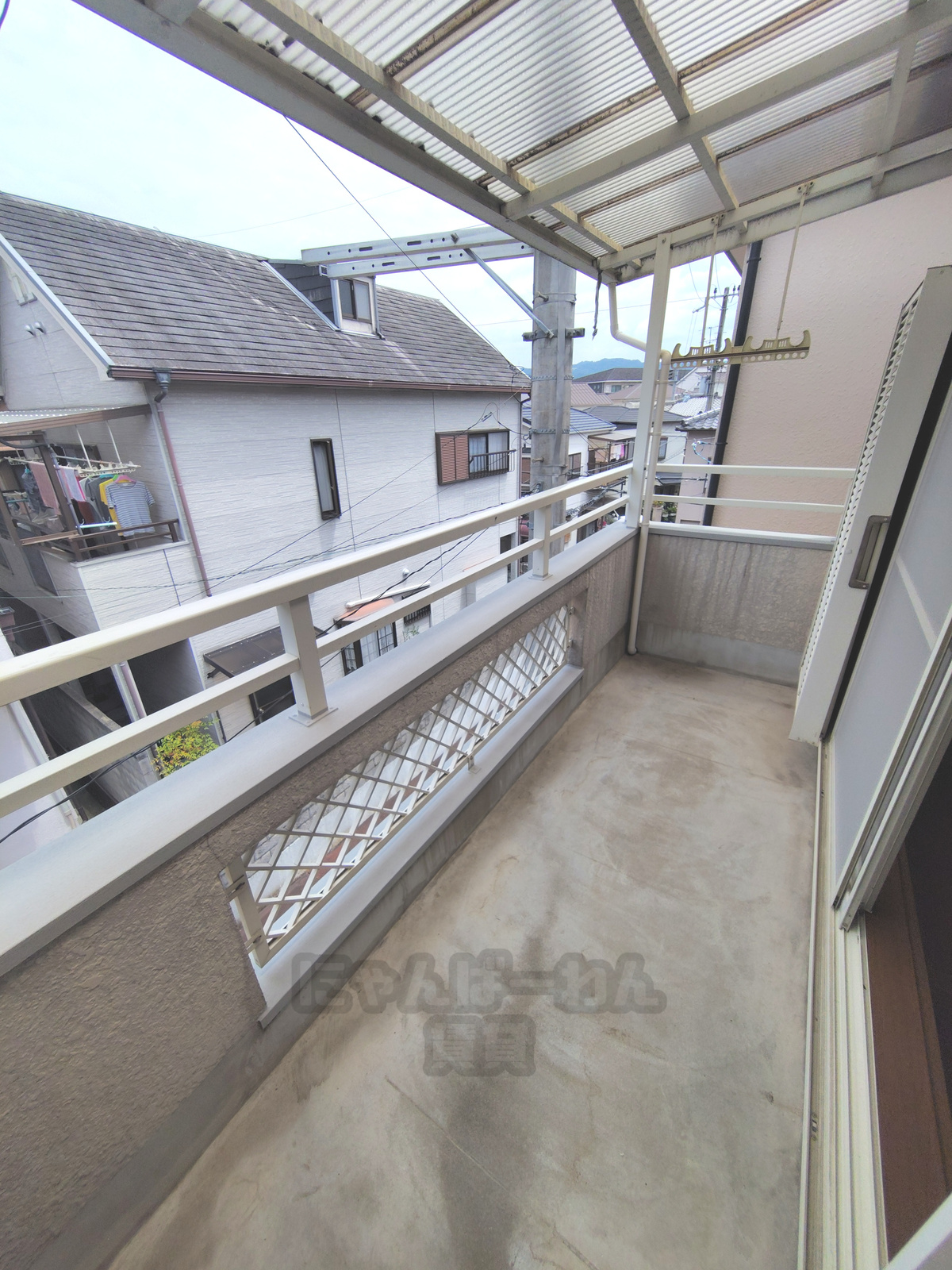 京都府宇治市宇治池森のペット可賃貸物件のベランダ。コンクリート床に、金属製の柵、屋根、物干し竿をかける金物が設置されています。